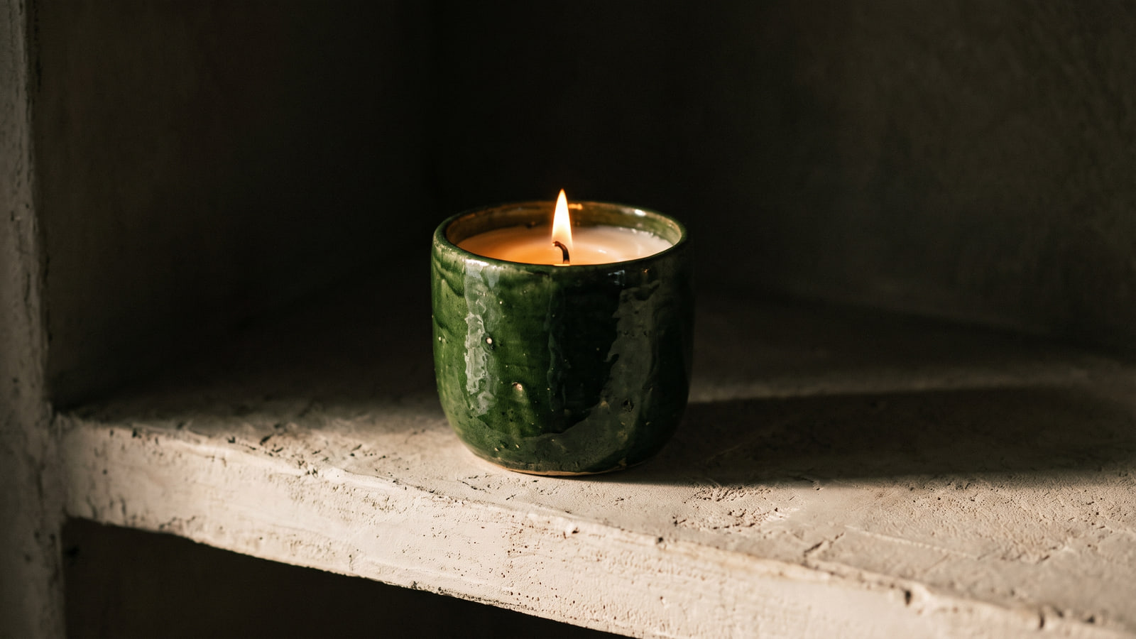 Loewe style glazed earthenware candle in deep green on a pale plaster shelf